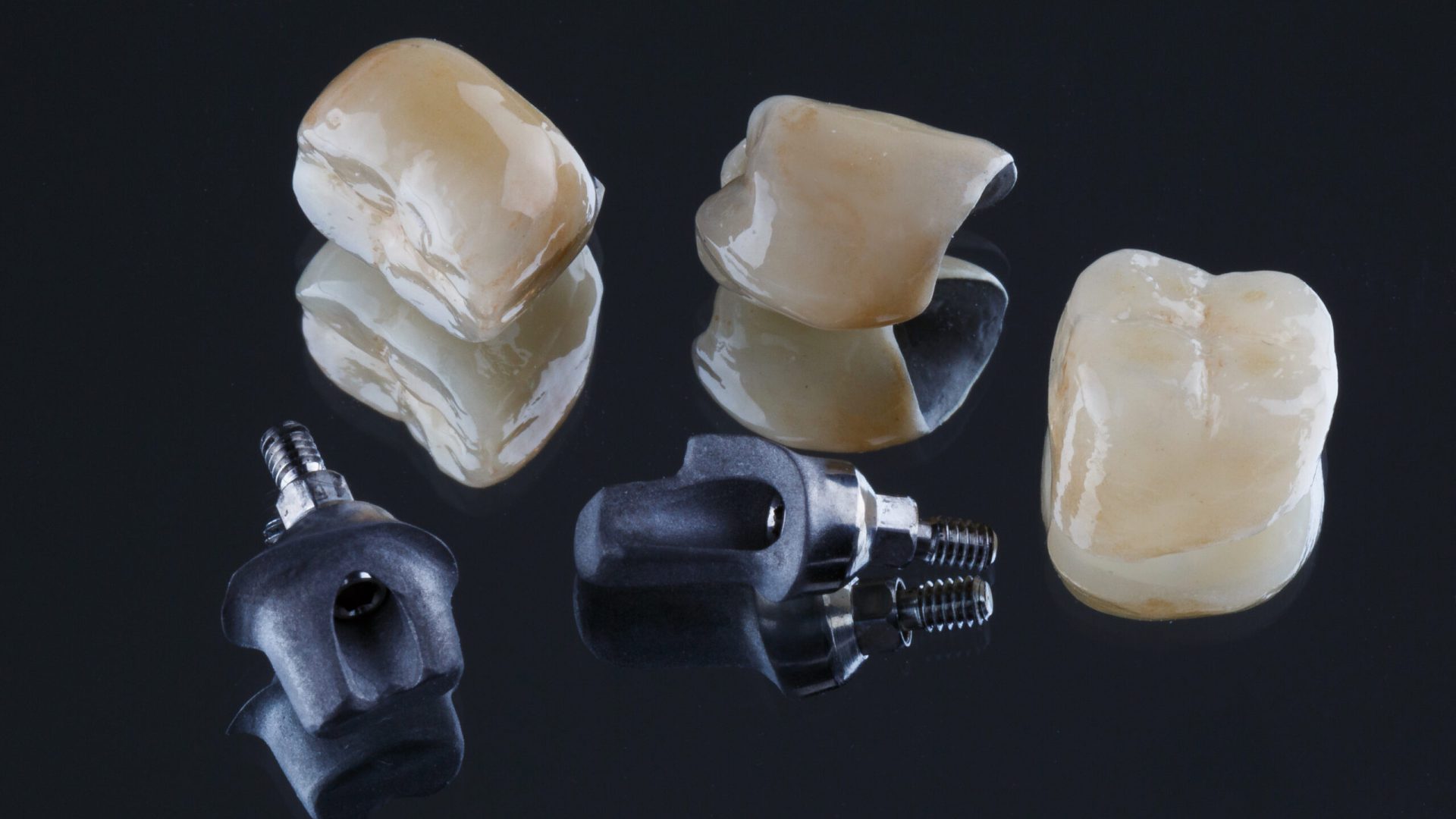 Dental crowns and three titanium base for installation, photographed on a mirror