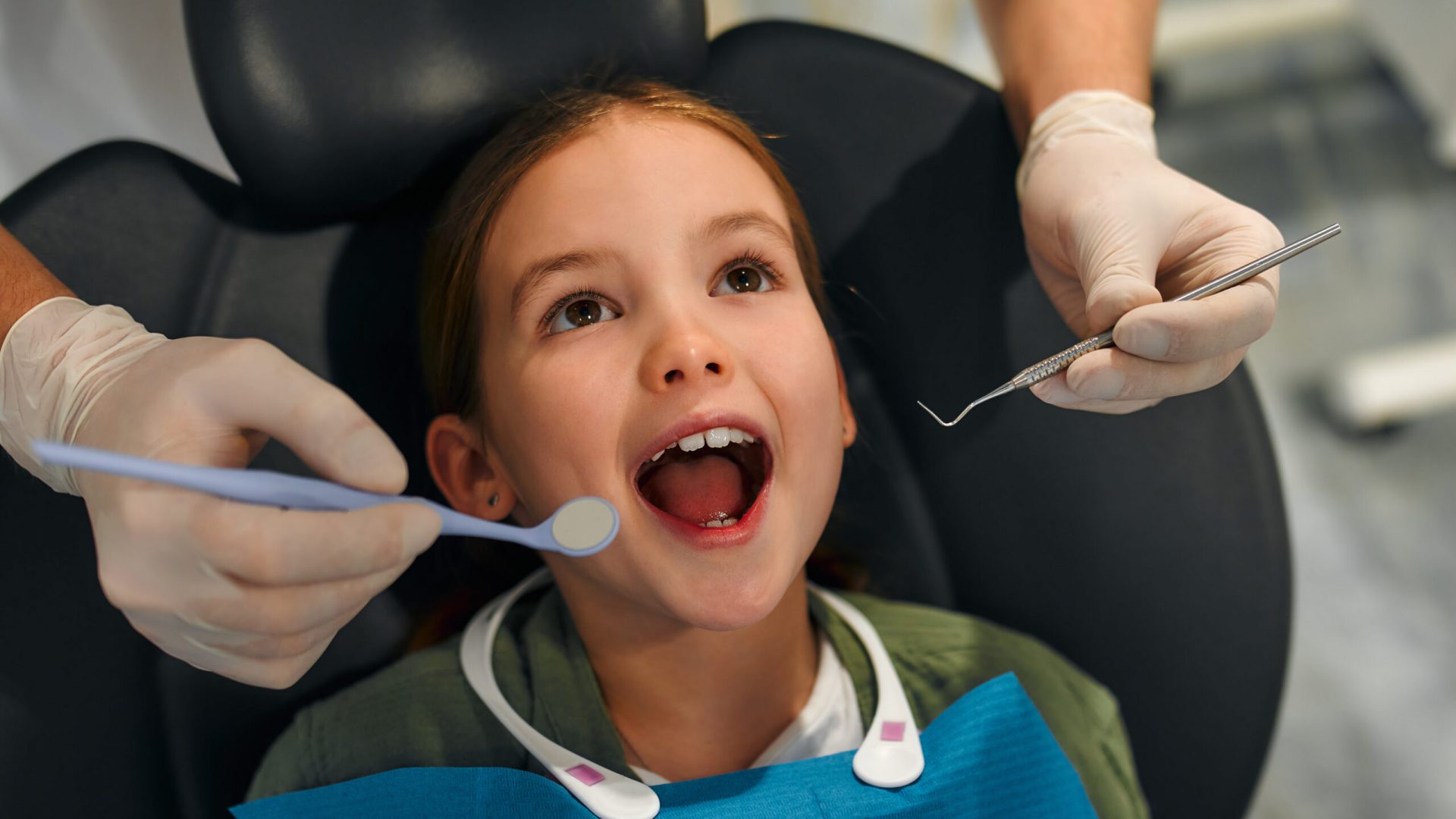 Child little girl sitting on a dental chair opening her mouth wide on examination by a pediatric dentist in a dental clinic. Dentistry and care of milk teeth.